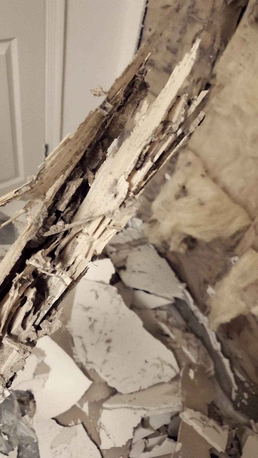 An opened wall with framing split into long splinters through its depth, fiberglass insulation and broken pieces of drywall alongside it.